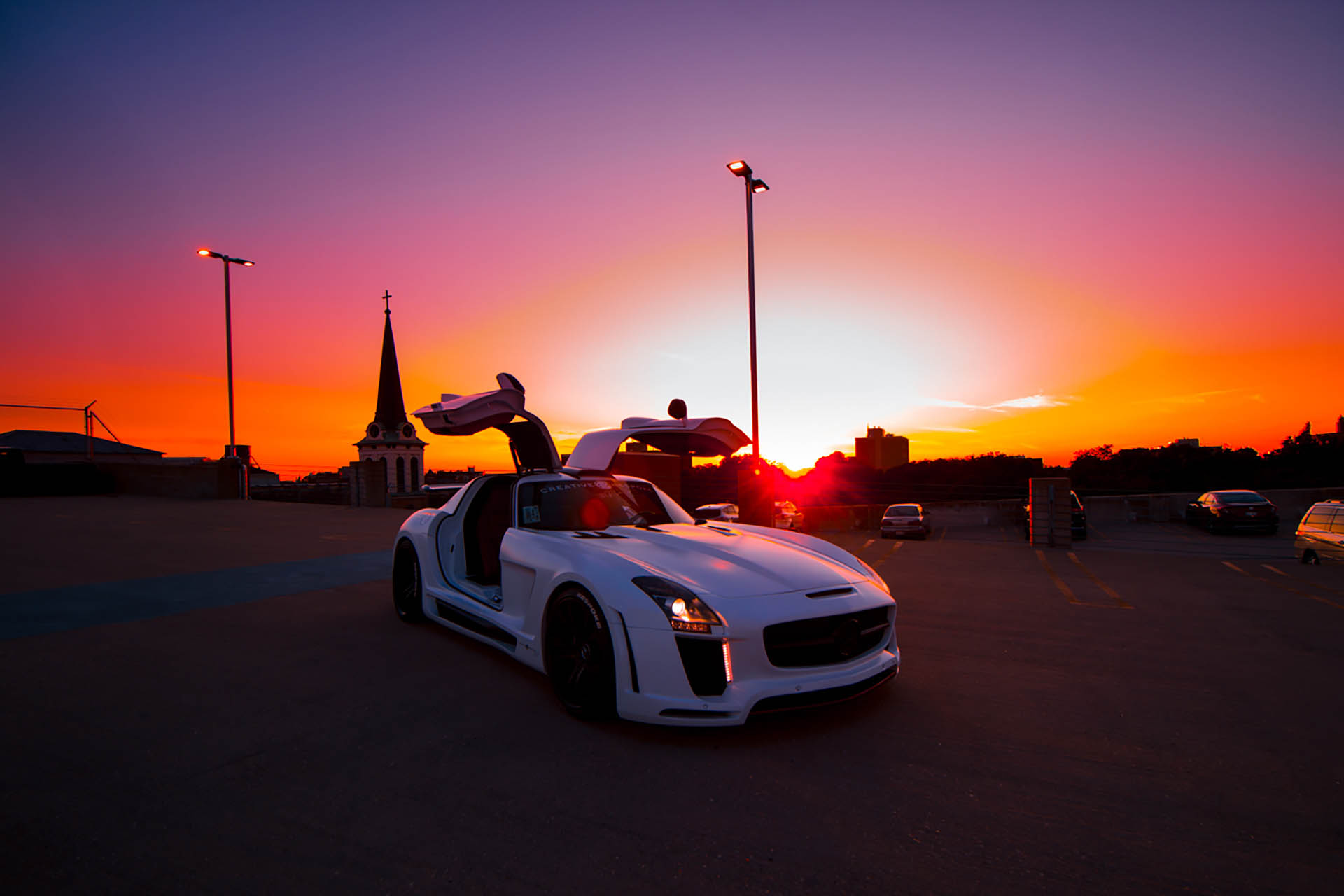 Colorful sunset over a white luxury car in a parking garage.