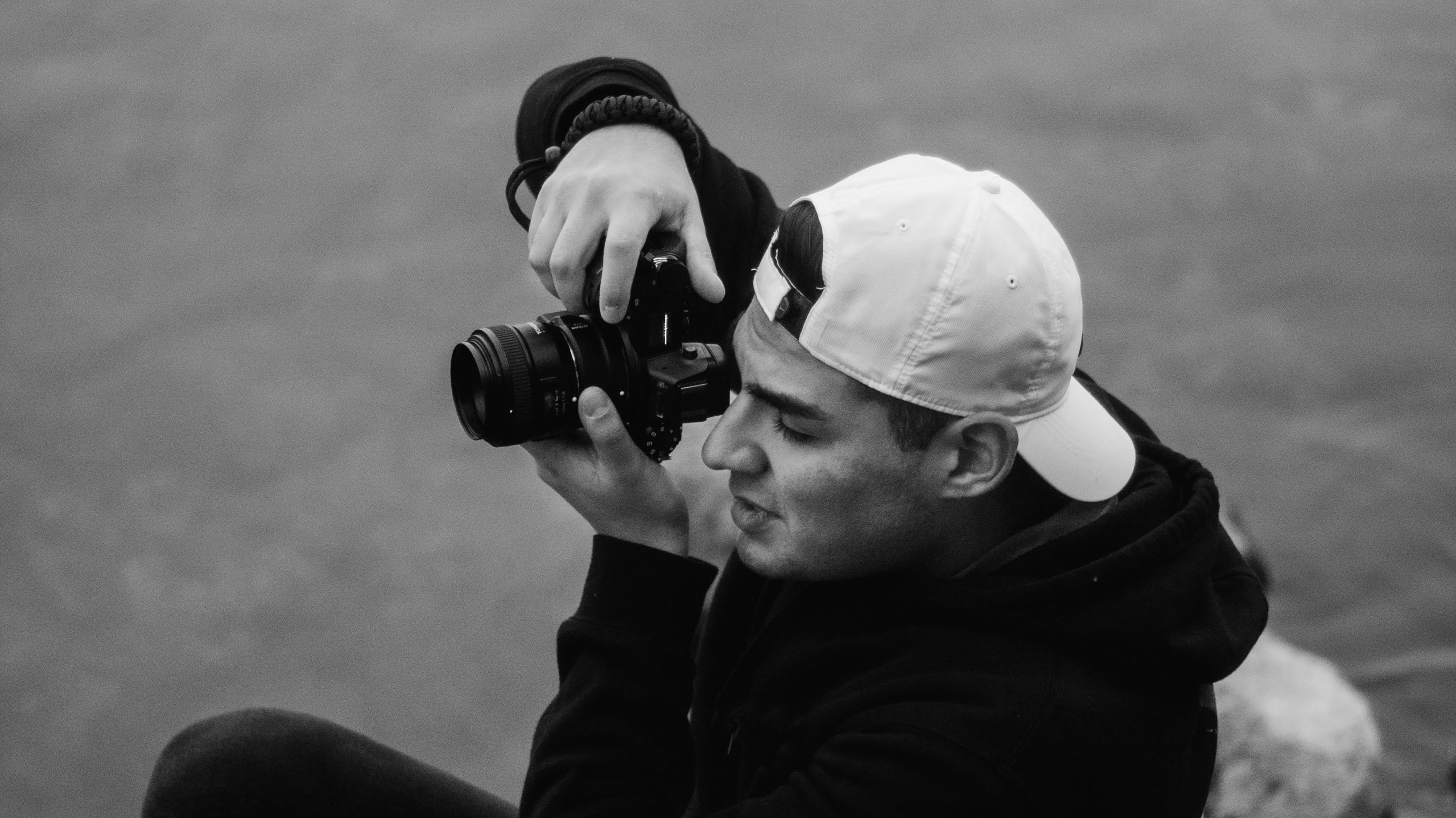 Photographer holding camera next to lake black and white
